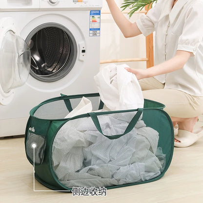 Green mesh laundry basket with side pocket, used for sorting clothes near washing machine