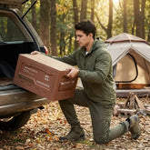 Man loading an outdoor camping storage box into a car trunk in a forested campsite setting.