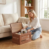 A woman organizing items in an outdoor camping storage box with a wooden lid, placed in a cozy living room.